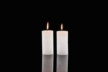 two burning white candles glowing isolated on black clipart