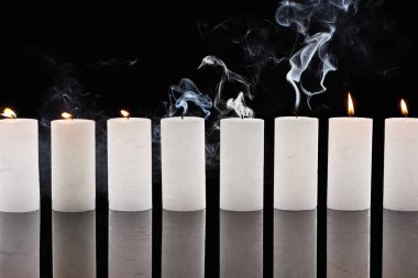 burning and extinct white candles with smoke on black background clipart