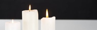 burning white candles on white surface glowing isolated on black, panoramic shot clipart
