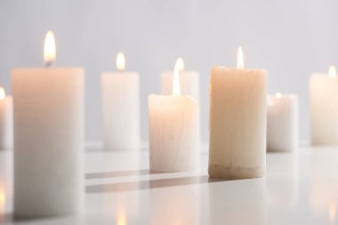 selective focus of burning white candles on white surface glowing isolated on grey clipart