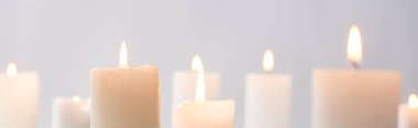 selective focus of burning white candles glowing isolated on grey, panoramic shot clipart