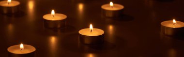 selective focus of burning white candles glowing in dark, panoramic shot clipart
