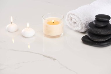 Spa taşlarının yanındaki camlarda beyaz mumlar yakmak ve mermer beyaz yüzeyde yuvarlanan havlular.