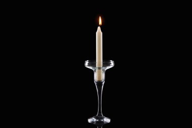 burning white candle glowing in glass candlestick isolated on black clipart