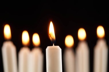 selective focus of burning white candle glowing isolated on black clipart