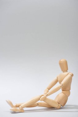 Elleri dizinin üstünde olan tahta bebek. Gri arka planda. Kopya alanı var.