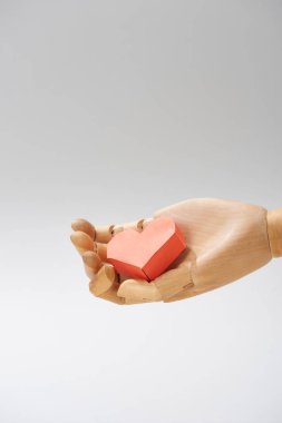 Gri renkte izole edilmiş oyuncak bebeğin ahşap elinde kalp şeklinde kağıt.