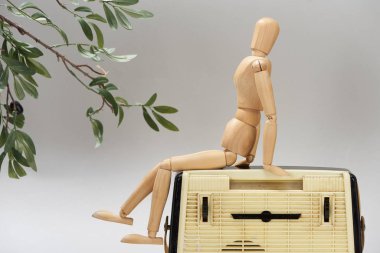 Wooden doll on vintage radio beside plant isolated on grey clipart