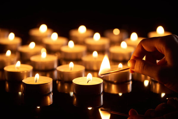 selective focus of woman lighting up candle with match in dark