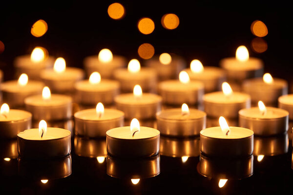 selective focus of burning candles glowing in darkness with bokeh lights