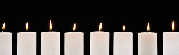 burning white candles glowing in line isolated on black, panoramic shot