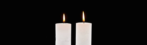 two burning white candles glowing isolated on black, panoramic shot