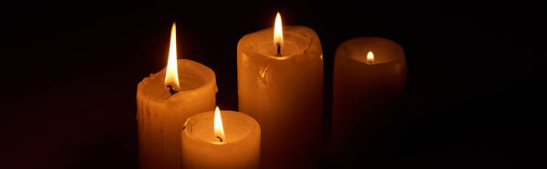burning candles glowing in darkness on black background, panoramic shot