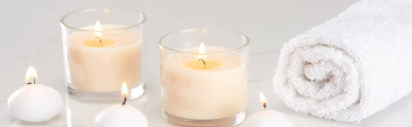 burning white candles in glass and rolled towel on marble white surface, panoramic shot