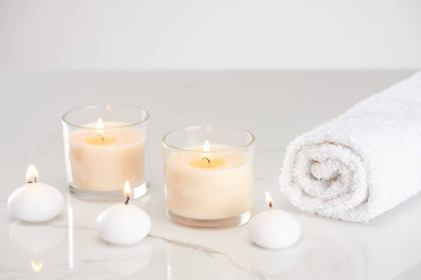 burning white candles in glass and rolled towel on marble white surface