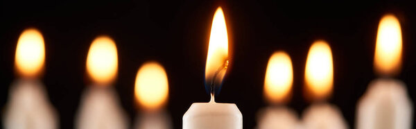 selective focus of burning white candle glowing isolated on black, panoramic shot