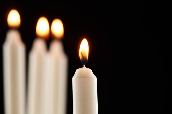selective focus of burning white candle glowing isolated on black