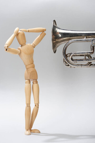 Wooden puppet with hands by head and alto horn on grey background