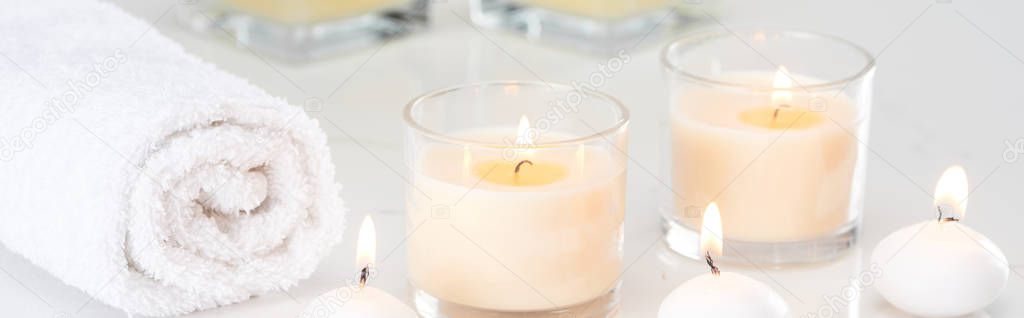 burning white candles in glass and rolled towel on marble white surface, panoramic shot