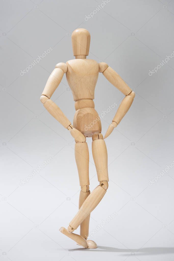 Wooden doll with hands on hips on grey background