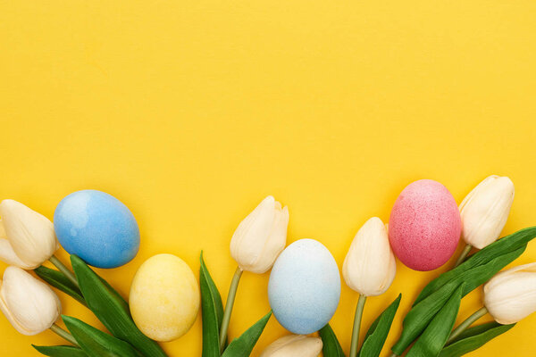 top view of tulips and painted Easter eggs on colorful yellow background
