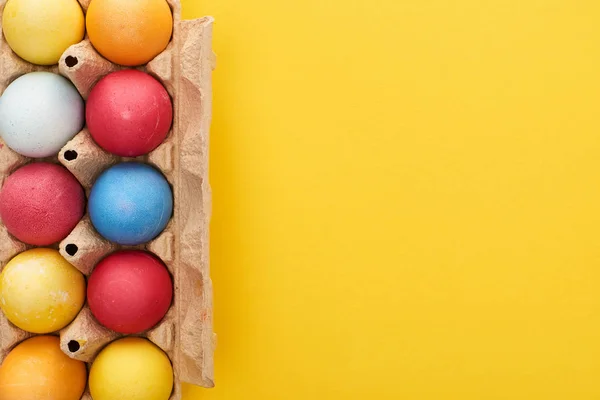 Vista Superior Ovos Páscoa Pintados Multicoloridos Recipiente Papelão Fundo Amarelo — Fotografia de Stock