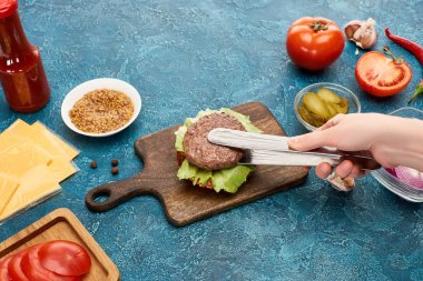 Mavi desenli yüzeyde enfes taze hamburger pişiren kadın manzarası.