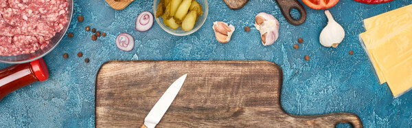 вид сверху на свежие ингредиенты бургера и деревянную разделочную доску с ножом на голубой текстурированной поверхности, панорамный снимок
