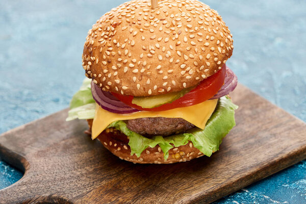 delicious cheeseburger on wooden board on blue textured surface