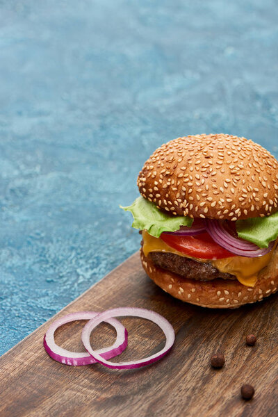 delicious cheeseburger on wooden board with onion on blue textured surface