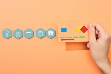 cropped view of woman holding credit card template on peach background with icons illustration