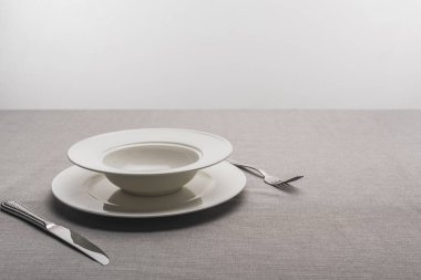 Çatal ve bıçaklı tabaklar gri arkaplanda masa örtüsü.