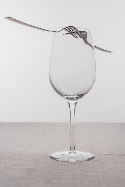 Çatallar boş şarap kadehinde, masa örtüsü gri renkte.