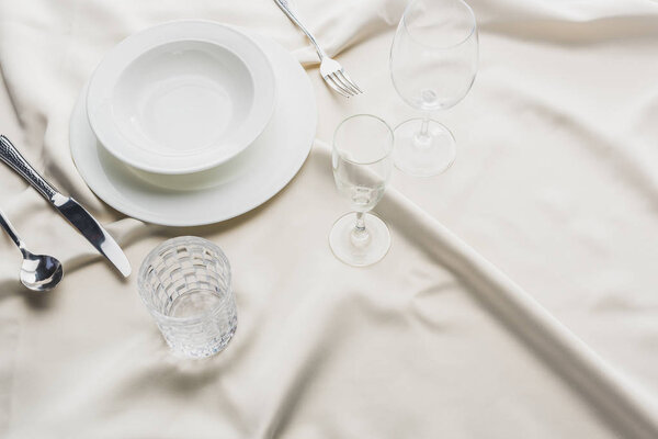 High angle view of serving tableware with glasses on white tablecloth