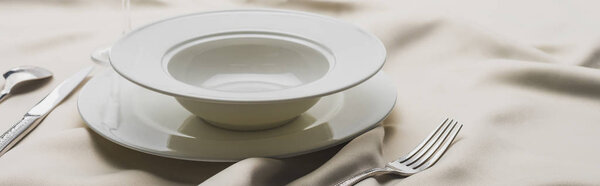 Panoramic shot of plates and cutlery on wavy white tablecloth