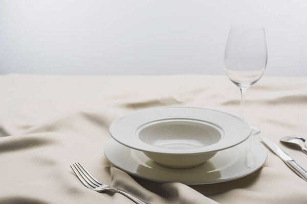 Селективный фокус тарелок и бокала вина на скатерти на сером фоне
