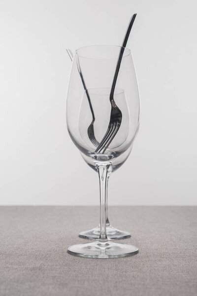 Селективный фокус вилок в прозрачных бокалах вина на скатерти, изолированных на сером
