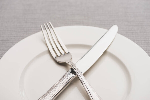 Close up view of fork and knife on empty plate on grey surface