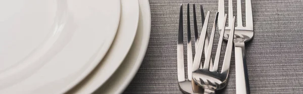 Panoramic shot of forks beside empty plates on grey surface