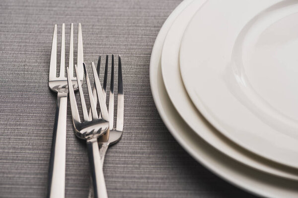 Empty plates with forks on grey linen tablecloth
