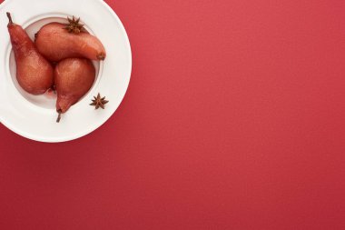 Kırmızı zemin üzerinde anason tabağı olan şaraplı armut manzarası.