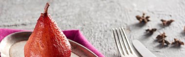 delicious pear in wine with anise on silver plate on grey concrete surface with pink napkin, knife and fork, panoramic shot clipart