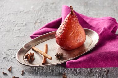 delicious pear in wine with cinnamon and anise on silver plate on grey concrete surface with pink napkin clipart