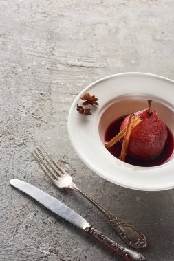 delicious pear in red wine with cinnamon and anise on plate on grey concrete surface with cutlery clipart