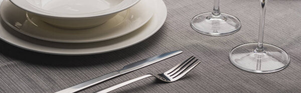 Serving plates with cutlery and wine glasses on grey cloth, panoramic shot