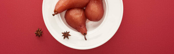 top view of delicious pear in wine with anise on plate on red background, panoramic shot