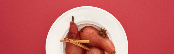 top view of delicious pear in wine with cinnamon and anise on plate on red background, panoramic shot