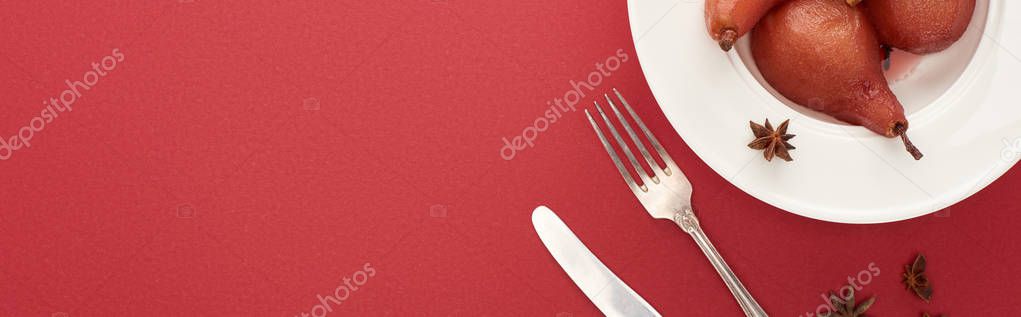 top view of delicious pear in wine with cinnamon and anise on plate on red background with cutlery, panoramic shot