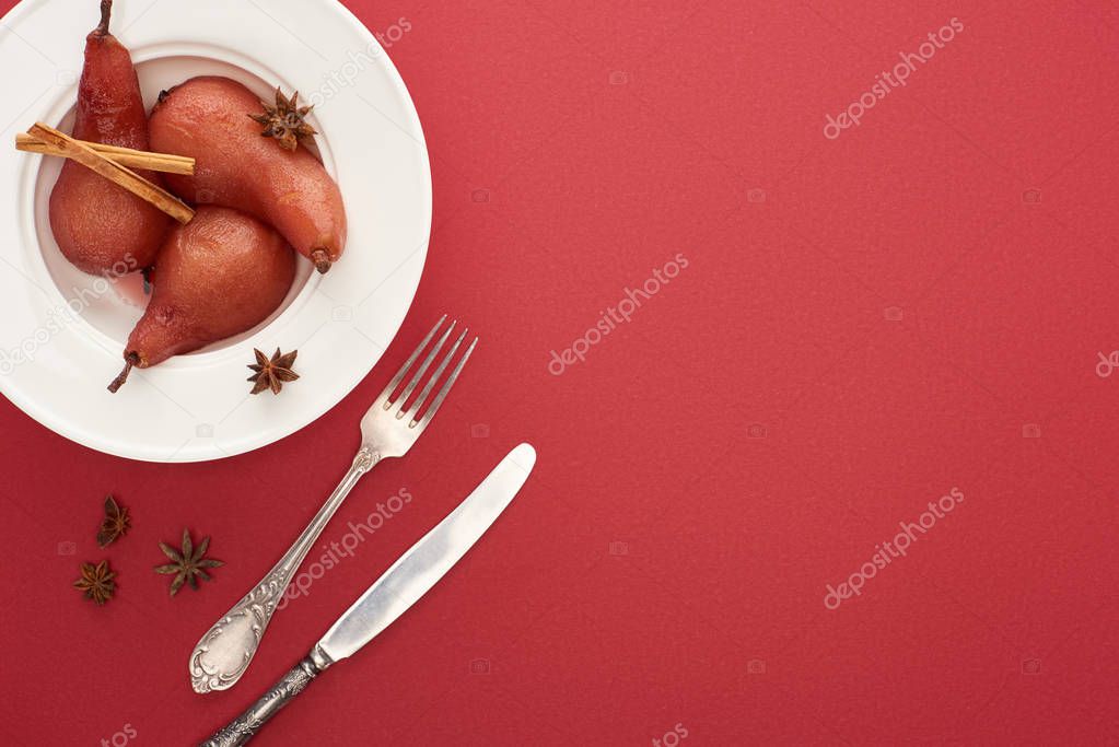 top view of delicious pear in wine with cinnamon and anise on plate on red background with cutlery