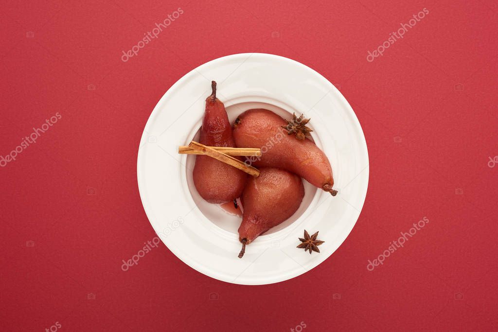 top view of delicious pear in wine with cinnamon and anise on plate on red background